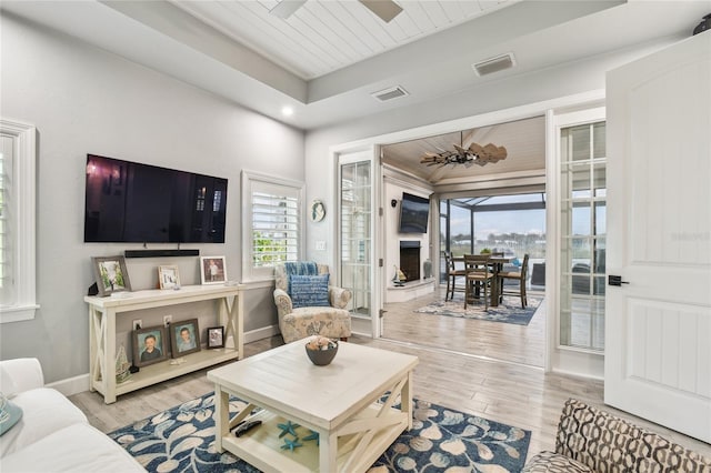 living room with a tray ceiling, wood ceiling, ceiling fan, and light wood-type flooring