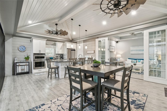 dining space featuring lofted ceiling with beams, ceiling fan, light wood-type flooring, and wood walls