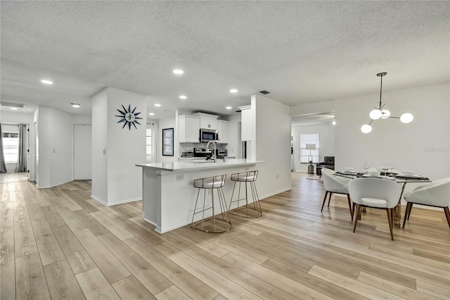 kitchen featuring sink, white cabinets, hanging light fixtures, kitchen peninsula, and light wood-type flooring