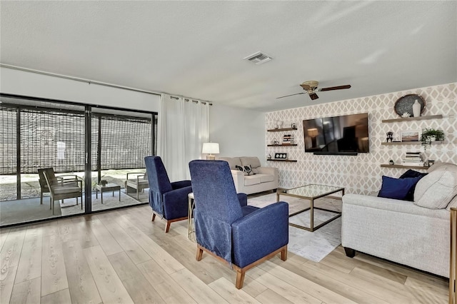 living room featuring ceiling fan, light hardwood / wood-style floors, and a textured ceiling