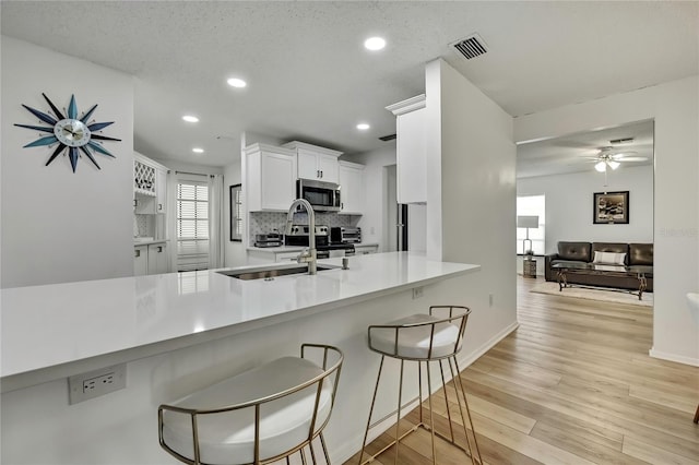 kitchen featuring a kitchen bar, kitchen peninsula, light hardwood / wood-style flooring, and white cabinets