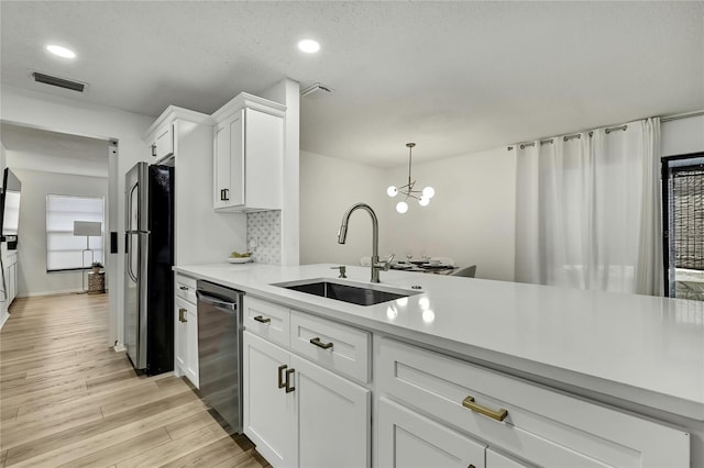 kitchen featuring appliances with stainless steel finishes, decorative light fixtures, sink, white cabinets, and light hardwood / wood-style floors