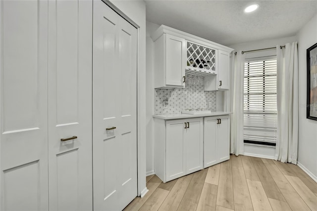 kitchen featuring white cabinetry, a textured ceiling, light hardwood / wood-style floors, and decorative backsplash