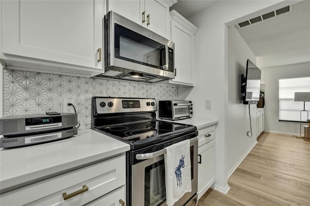 kitchen with stainless steel appliances, white cabinetry, light wood-type flooring, and decorative backsplash