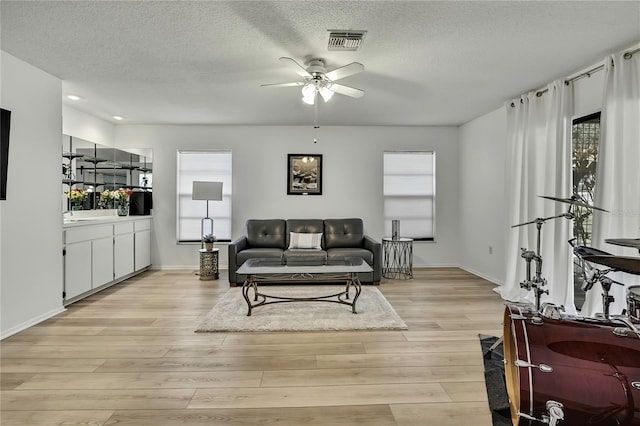 living room featuring ceiling fan, a textured ceiling, and light hardwood / wood-style floors