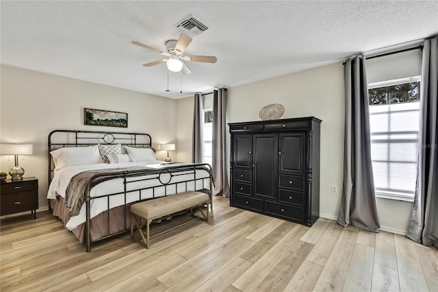 bedroom with multiple windows, ceiling fan, light hardwood / wood-style flooring, and a textured ceiling