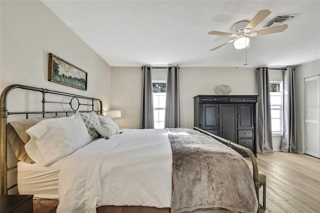 bedroom with ceiling fan, a textured ceiling, multiple windows, and light hardwood / wood-style flooring