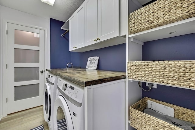 clothes washing area with cabinets, washing machine and dryer, a textured ceiling, and light hardwood / wood-style floors