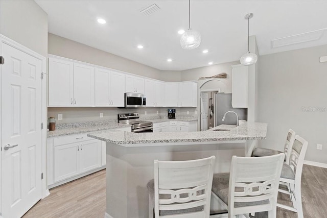 kitchen featuring white cabinetry, light stone counters, appliances with stainless steel finishes, pendant lighting, and light hardwood / wood-style floors