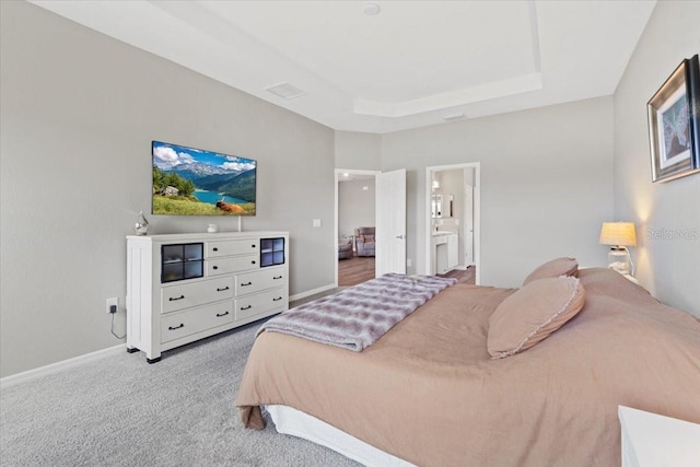 carpeted bedroom with a tray ceiling and connected bathroom