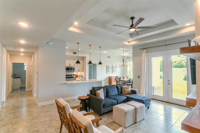 tiled living room with sink, ceiling fan with notable chandelier, a raised ceiling, and french doors