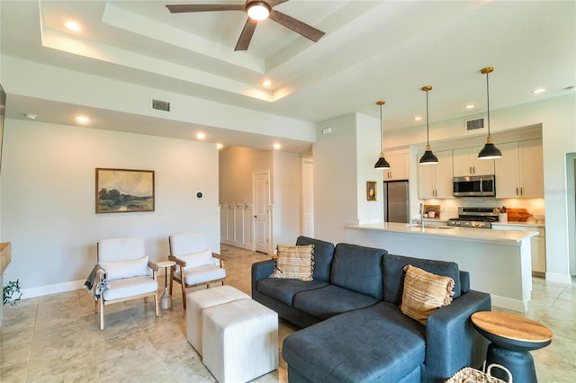 living room with sink, ceiling fan, and a tray ceiling