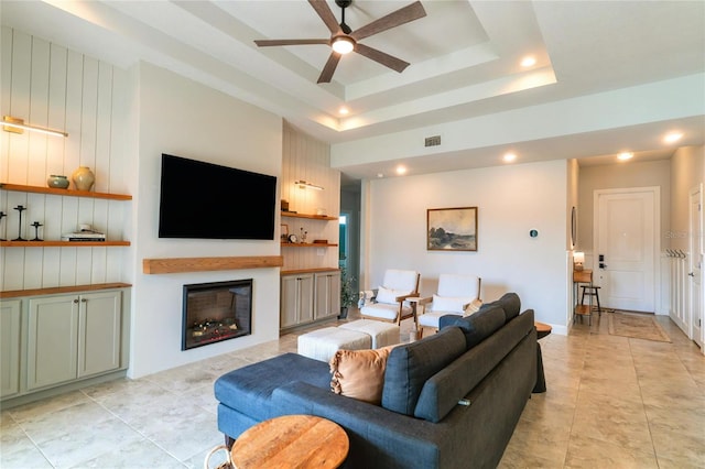 living room with light tile patterned floors, a raised ceiling, and ceiling fan