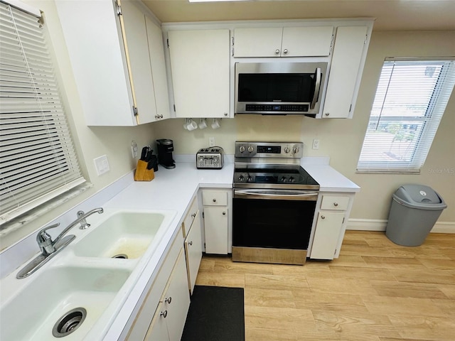 kitchen with stainless steel appliances, white cabinetry, sink, and light hardwood / wood-style flooring