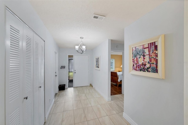 hallway with light tile patterned floors, a notable chandelier, and a textured ceiling