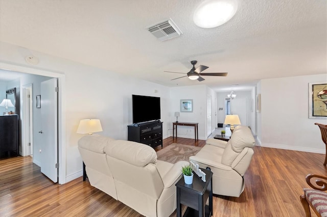 living room with hardwood / wood-style flooring, ceiling fan with notable chandelier, and a textured ceiling