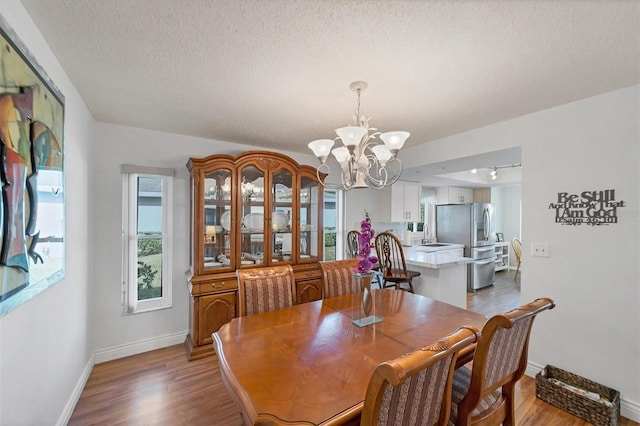 dining room with sink, a textured ceiling, light hardwood / wood-style flooring, and a notable chandelier