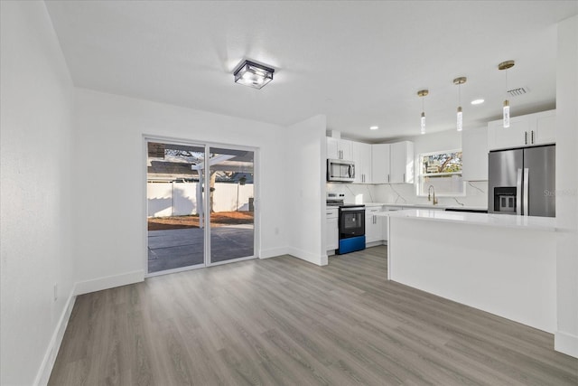 kitchen featuring appliances with stainless steel finishes, white cabinets, pendant lighting, hardwood / wood-style floors, and backsplash