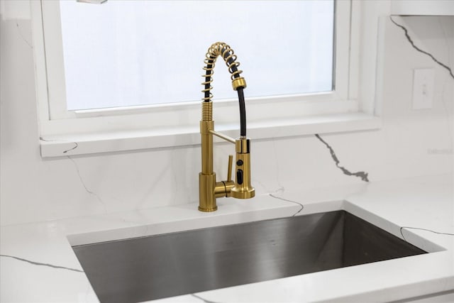 interior details featuring white cabinetry, sink, and light stone counters