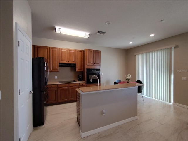 kitchen featuring extractor fan, light countertops, black appliances, brown cabinetry, and a center island with sink