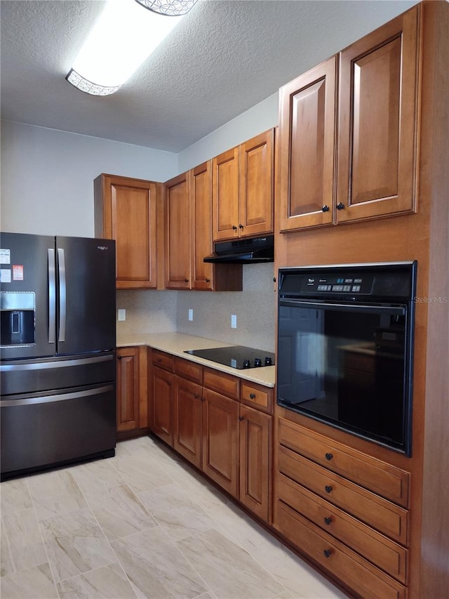 kitchen with brown cabinets, light countertops, a textured ceiling, under cabinet range hood, and black appliances