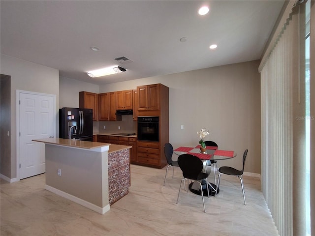 kitchen with visible vents, light countertops, black appliances, brown cabinetry, and a center island with sink