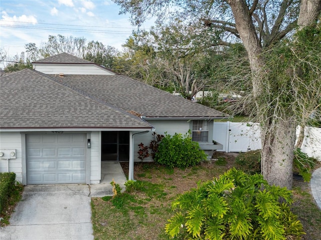 ranch-style home featuring a shingled roof, an attached garage, a gate, fence, and driveway