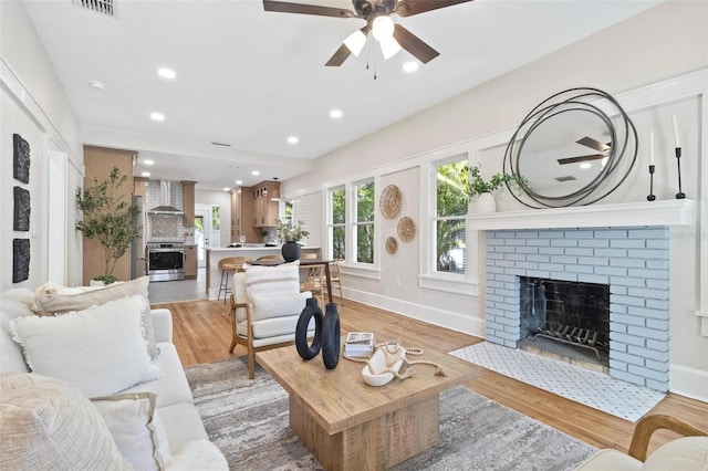 living room featuring ceiling fan, a fireplace, and light wood-type flooring