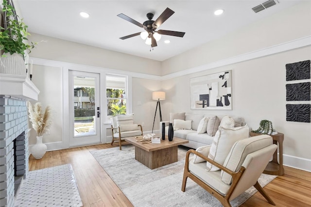 living room featuring ceiling fan, a fireplace, and light hardwood / wood-style floors