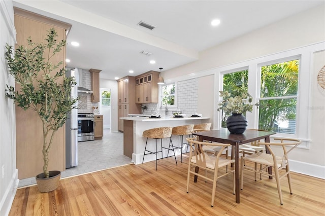 kitchen featuring stainless steel stove, tasteful backsplash, a kitchen bar, kitchen peninsula, and light hardwood / wood-style flooring