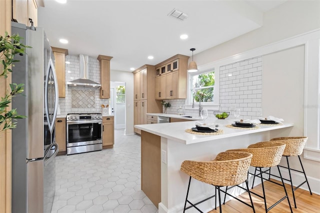 kitchen with wall chimney range hood, a breakfast bar, appliances with stainless steel finishes, hanging light fixtures, and kitchen peninsula