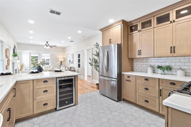 kitchen featuring stainless steel refrigerator, beverage cooler, decorative backsplash, ceiling fan, and light brown cabinets