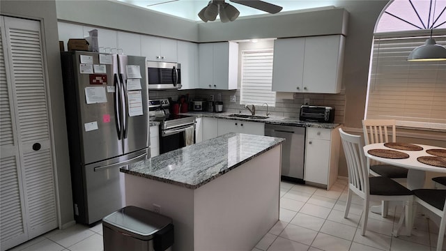 kitchen with white cabinetry, light stone counters, appliances with stainless steel finishes, a kitchen island, and decorative backsplash