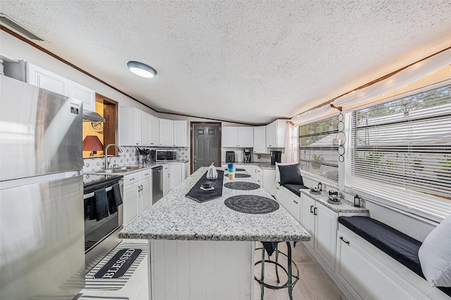 kitchen with a breakfast bar, appliances with stainless steel finishes, a kitchen island, light stone countertops, and white cabinets