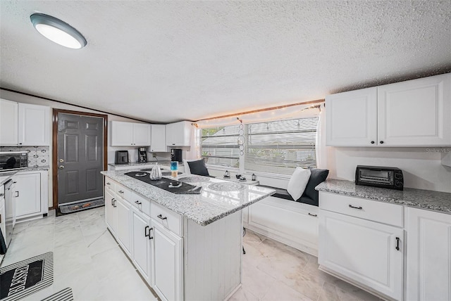 kitchen with white cabinetry, vaulted ceiling, a kitchen island, and a textured ceiling