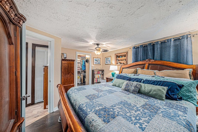 bedroom with a walk in closet, a textured ceiling, a closet, hardwood / wood-style flooring, and ceiling fan