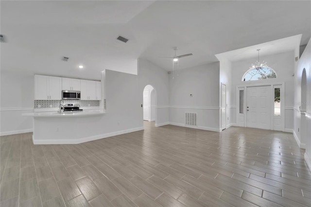 unfurnished living room featuring lofted ceiling and ceiling fan with notable chandelier