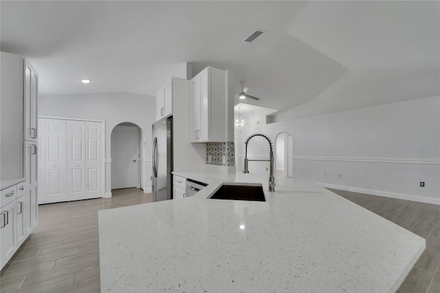 kitchen with appliances with stainless steel finishes, lofted ceiling, sink, kitchen peninsula, and light stone countertops