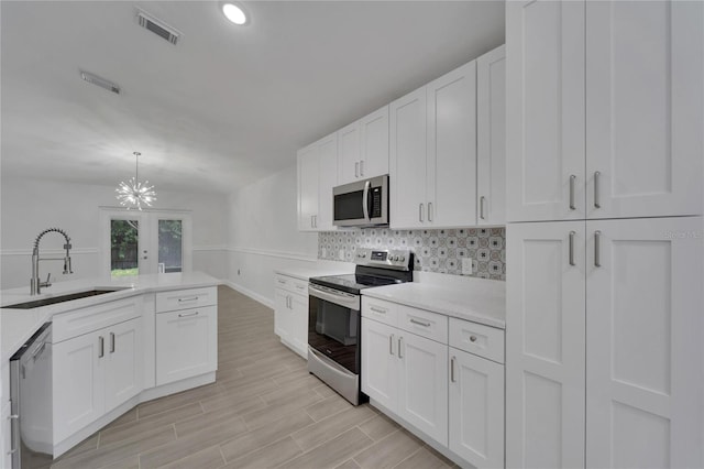 kitchen with decorative light fixtures, sink, white cabinets, decorative backsplash, and stainless steel appliances