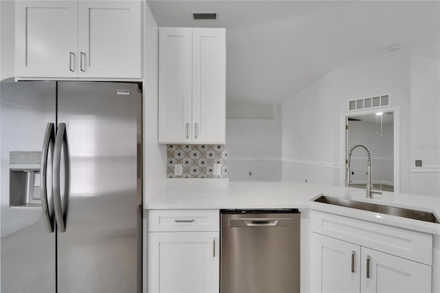 kitchen featuring sink, appliances with stainless steel finishes, white cabinetry, light stone counters, and decorative backsplash