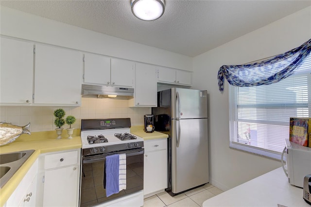 kitchen with white cabinetry, stainless steel fridge, decorative backsplash, light tile patterned floors, and gas stove