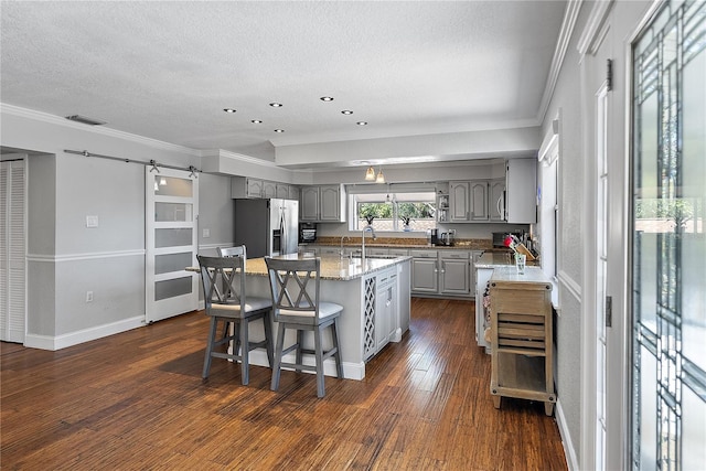 kitchen with gray cabinets, a kitchen island, a breakfast bar area, stainless steel fridge with ice dispenser, and a barn door