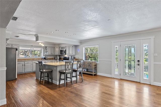 kitchen with a breakfast bar, dark hardwood / wood-style flooring, gray cabinets, a kitchen island, and stainless steel appliances