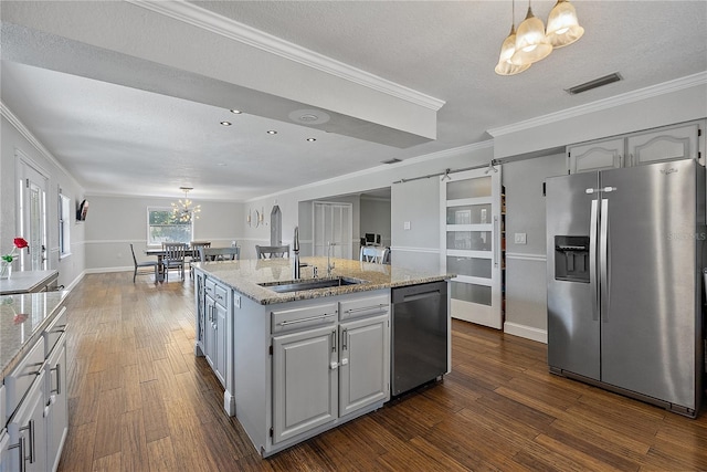 kitchen with pendant lighting, sink, stainless steel appliances, an island with sink, and a barn door