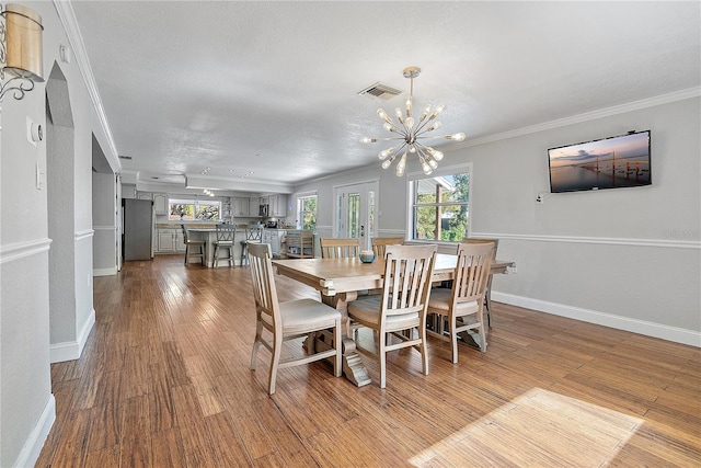 dining area featuring wood-type flooring, ornamental molding, and an inviting chandelier