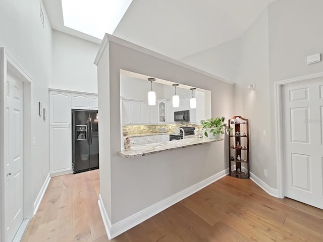 kitchen with black appliances, white cabinetry, decorative backsplash, kitchen peninsula, and light wood-type flooring