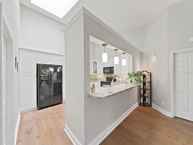 kitchen featuring a skylight, tasteful backsplash, white cabinetry, hanging light fixtures, and black appliances