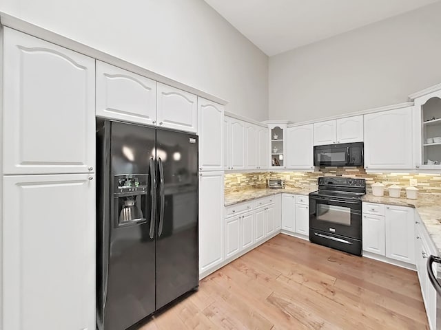 kitchen featuring white cabinets, decorative backsplash, a high ceiling, light stone counters, and black appliances