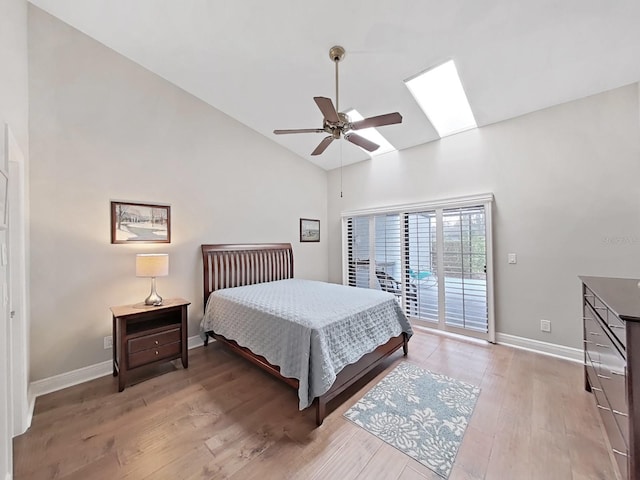 bedroom featuring hardwood / wood-style floors, high vaulted ceiling, a skylight, access to exterior, and ceiling fan