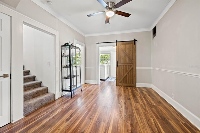 empty room with crown molding, a barn door, ceiling fan, and dark hardwood / wood-style flooring